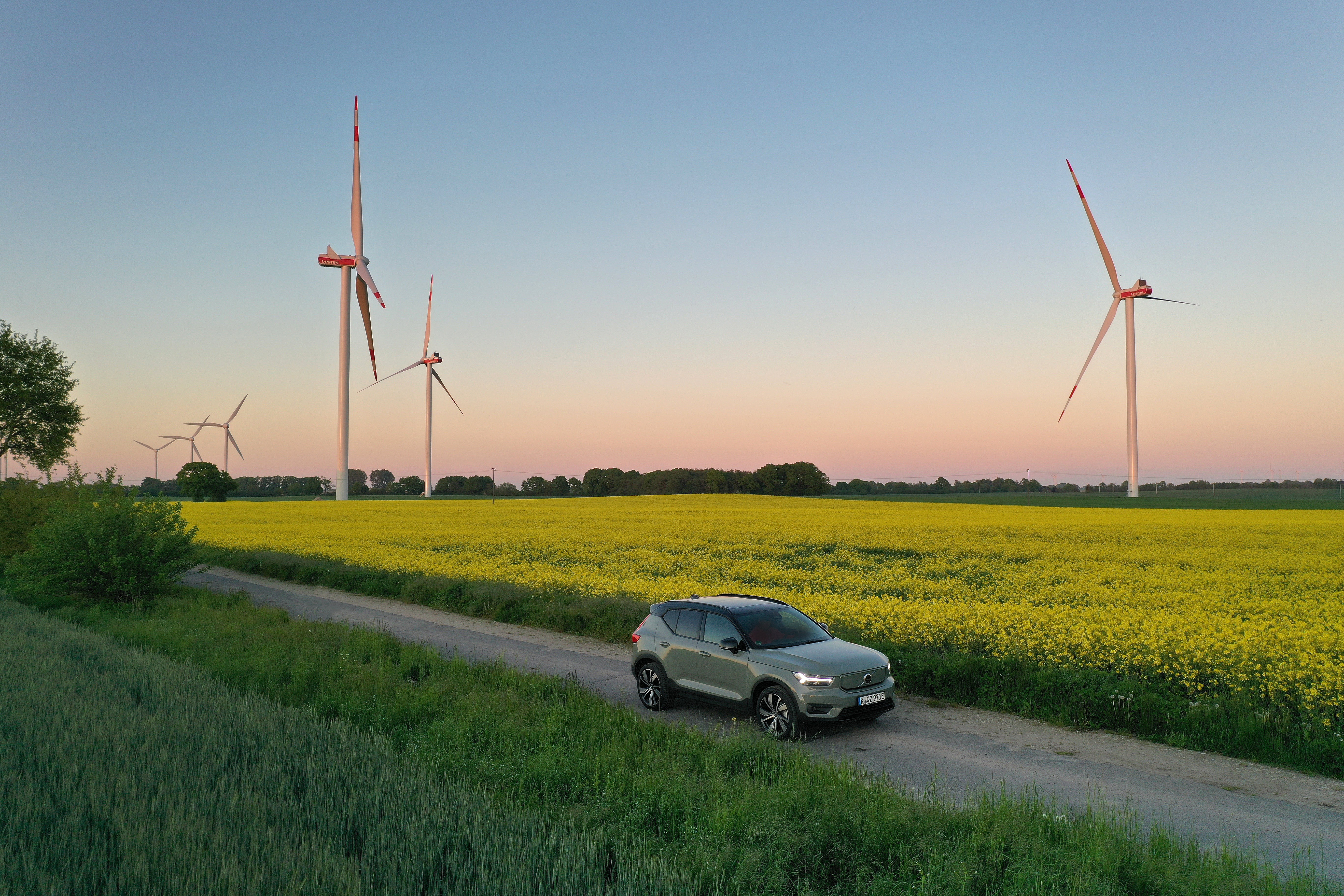 coche eléctrico conduciendo por una carretera rural con campos y molinos de viento detrás