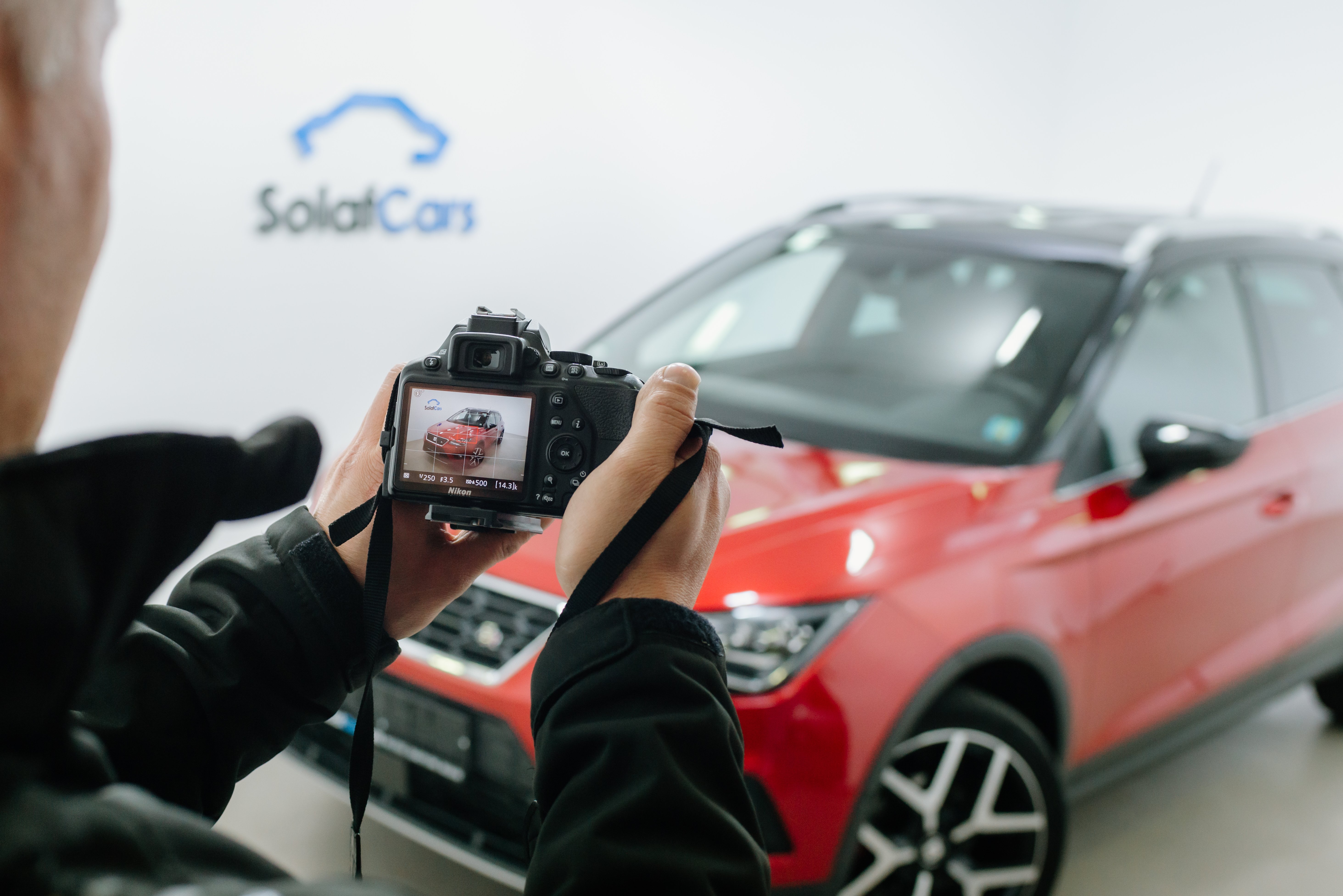 Primer plano de un hombre haciendo una foto con una cámara dslr a un coche rojo en un estudio fotográfico
